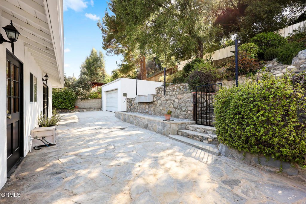 Stone-paved driveway beside a white house, with a detached garage and landscaped retaining wall.