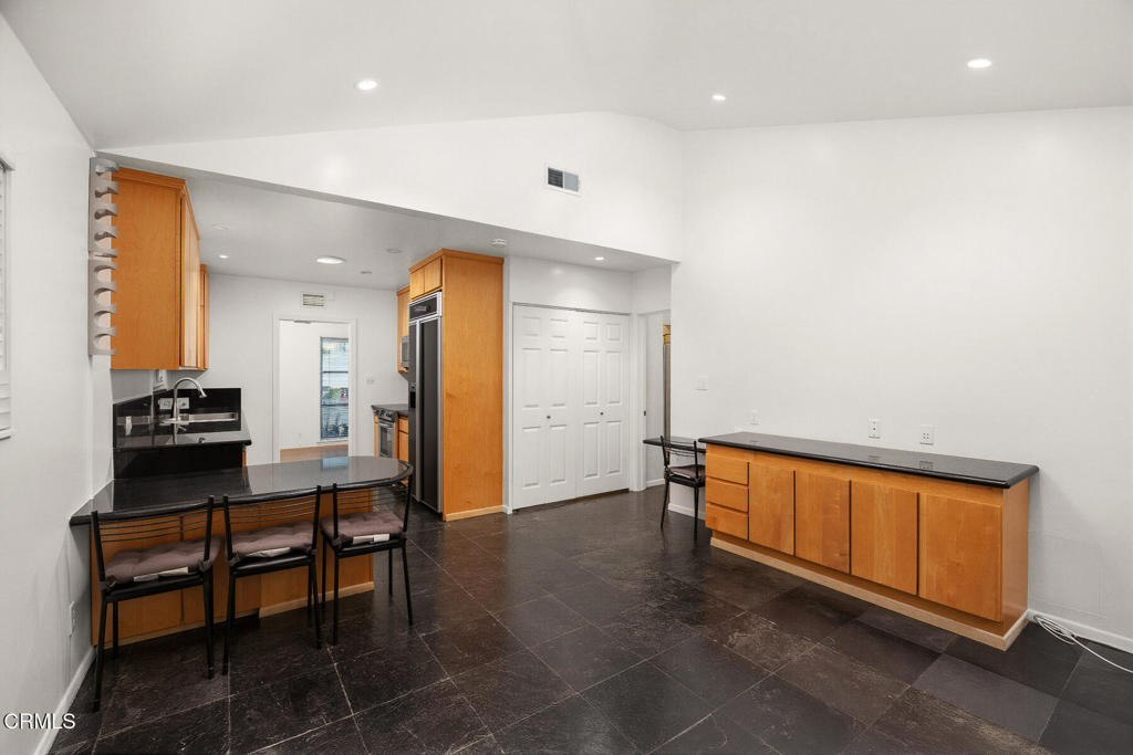 Kitchen with warm wood cabinetry, black counters, dark tile floors, and chairs at a breakfast peninsula.