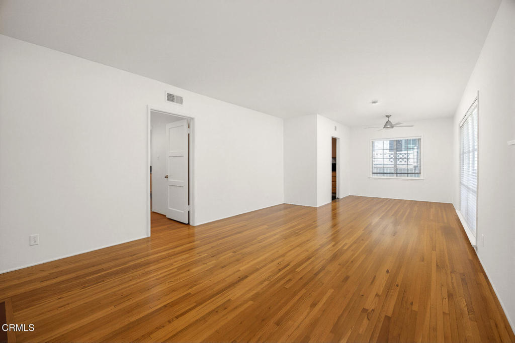 Vacant room with polished hardwood floors, white walls, a ceiling fan, and windows with blinds.