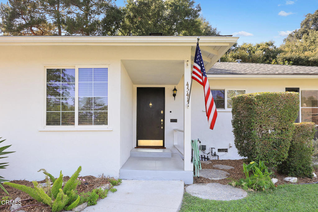 White single-story home with a covered entry, black front door, and American flag.