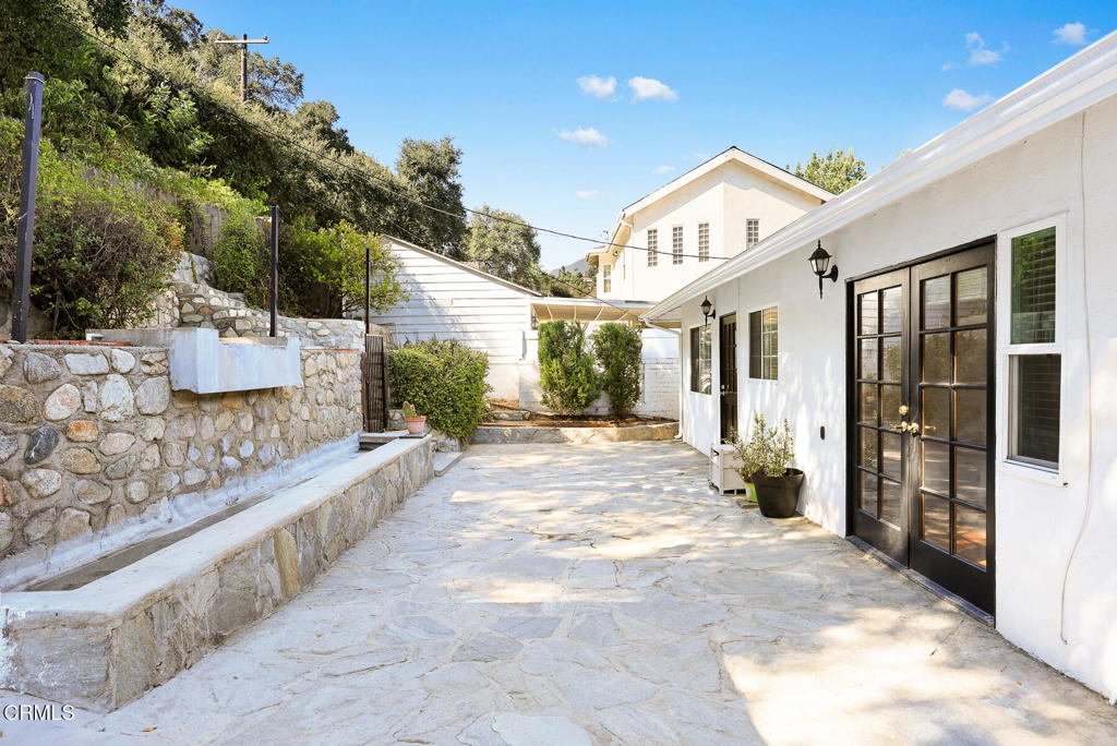 Stone courtyard beside a white home, with black double doors and a raised planting wall.