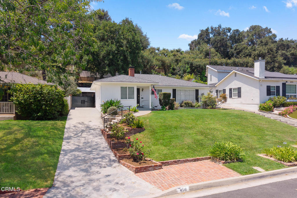 Single-story white home with a broad green lawn, brick-edged planting beds, and a concrete driveway.