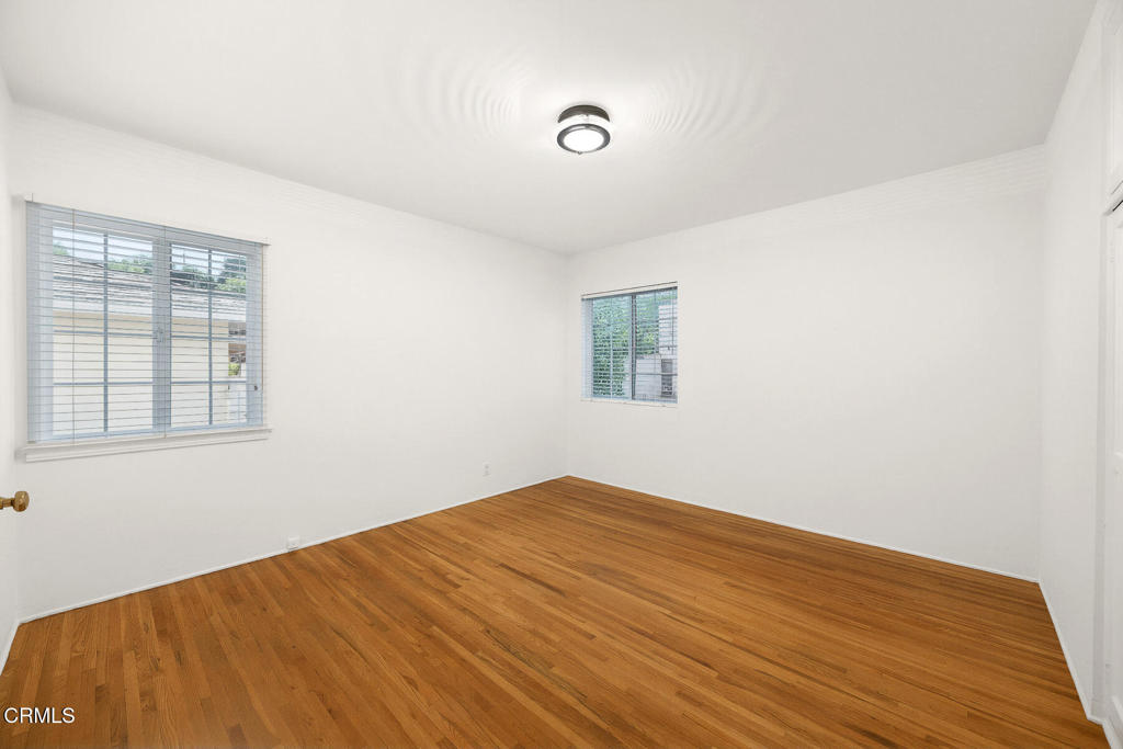 Empty room with hardwood floors, two windows with blinds, and a ceiling light.