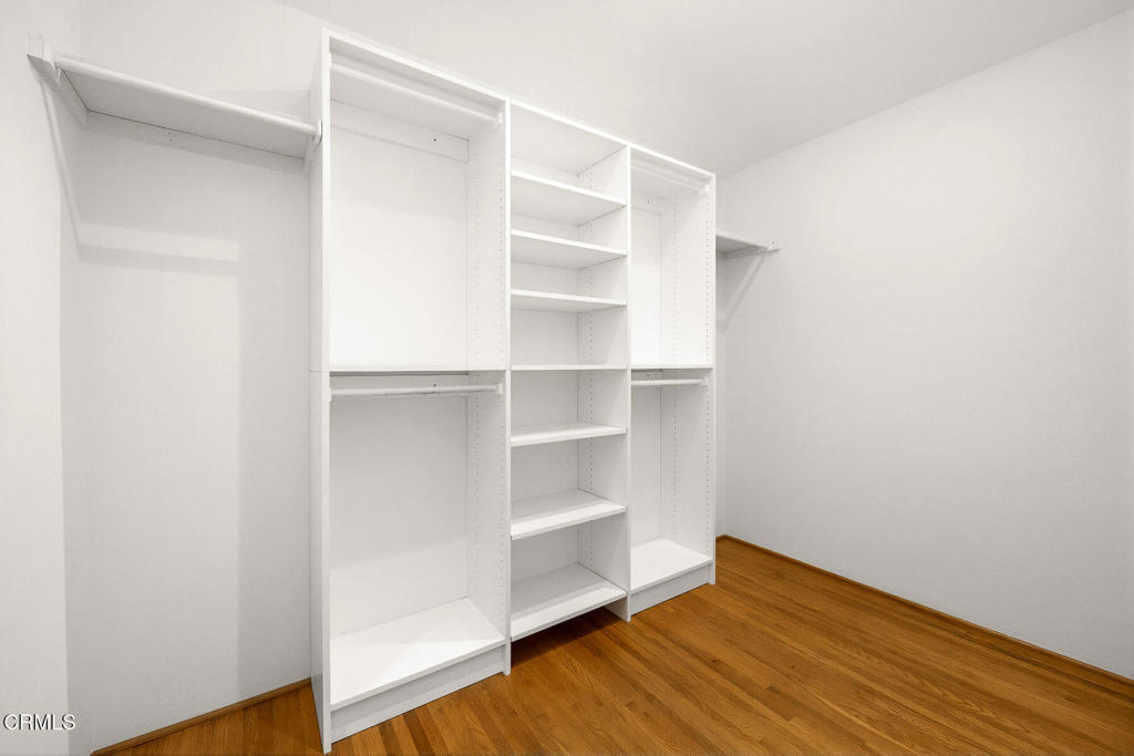 Walk-in closet with white built-in shelves and hanging areas over hardwood flooring.