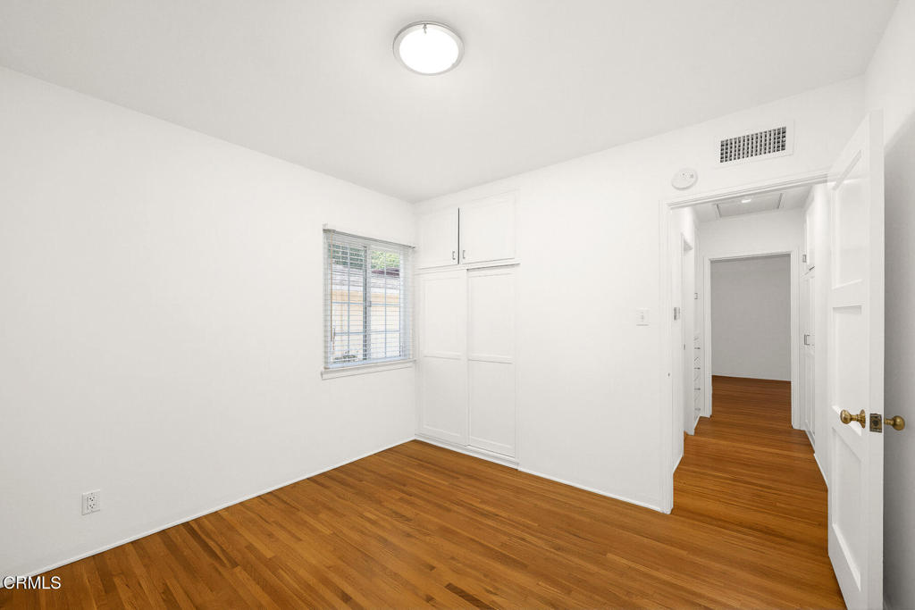 Empty bedroom with hardwood floors, a window, and a built-in closet.