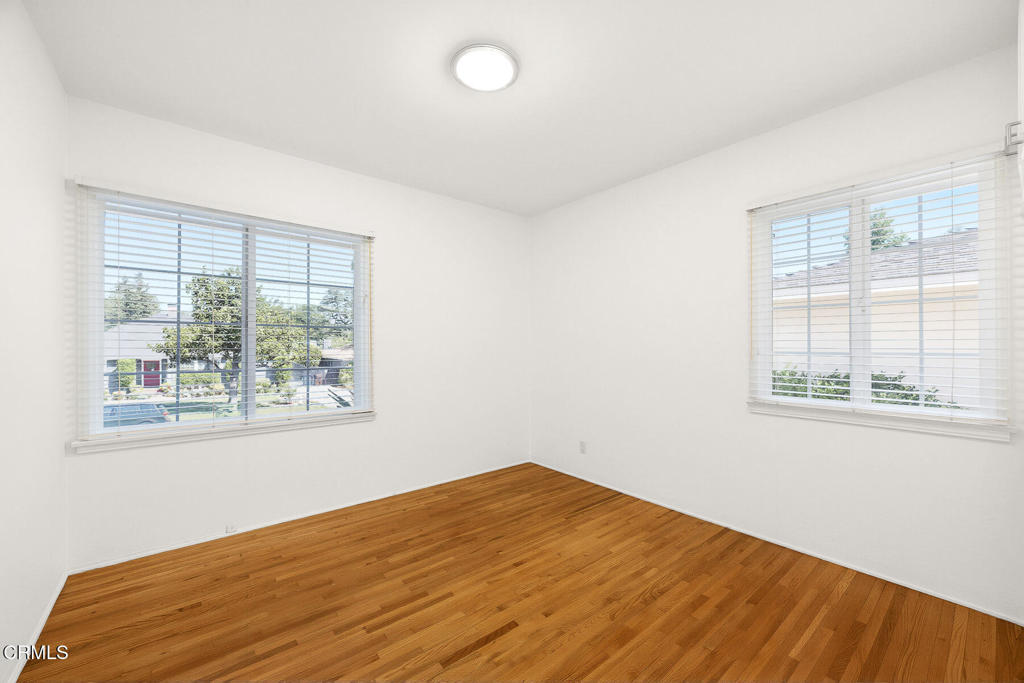 Vacant bedroom with hardwood floors and two windows with white blinds.