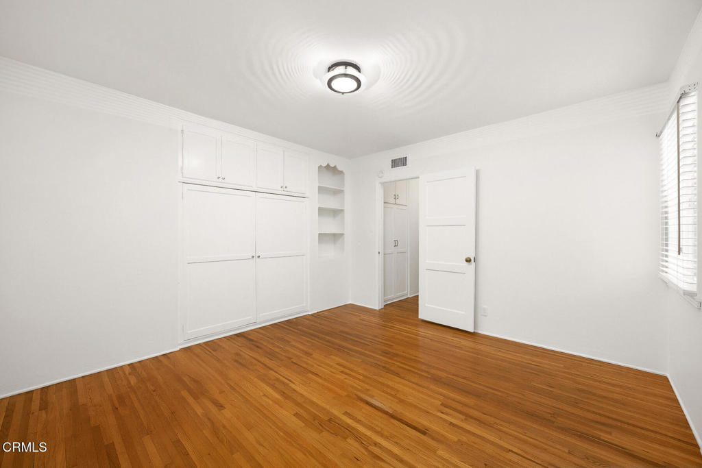 Unfurnished bedroom with built-in white closets, hardwood floors, and a window with blinds.