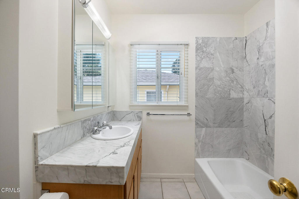 Bathroom with a marble vanity, white bathtub, and gray marble shower surround.