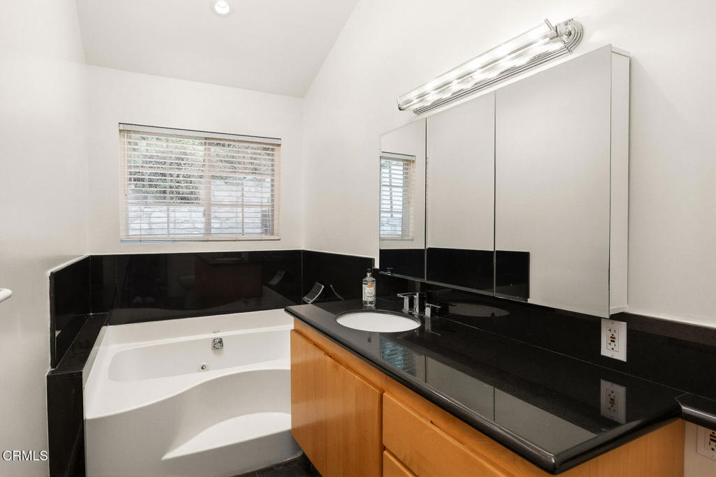 Bathroom with a corner jetted tub, black stone counters, and a wood vanity.