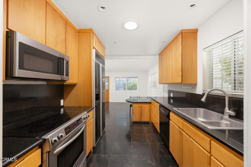 Kitchen with honey-colored wood cabinets, black countertops, stainless appliances, and a double-basin sink.
