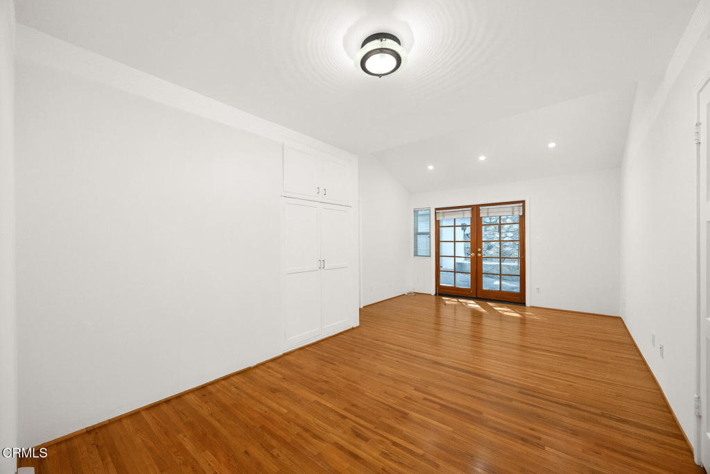 Empty bedroom with hardwood floors, built-in closets, and wood-framed glass doors.