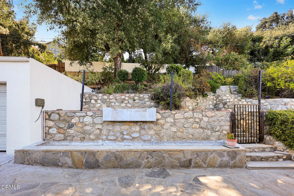 Stone retaining walls and a gated, landscaped hillside beside a paved driveway.