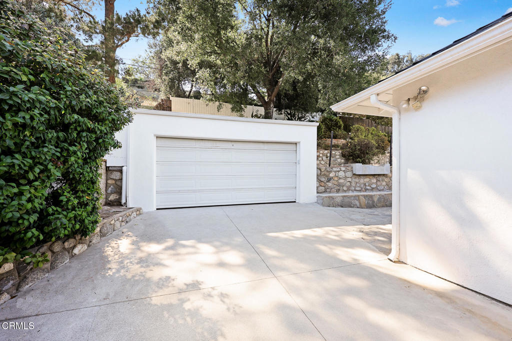 White detached garage with a closed double door, concrete driveway, and stone retaining walls.