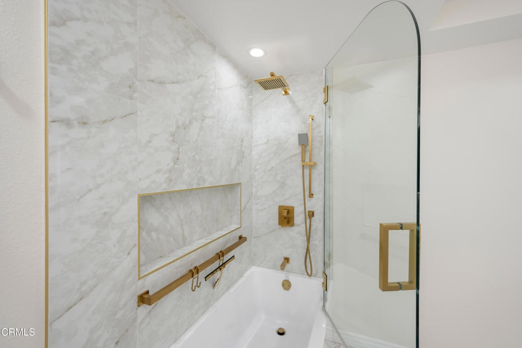 Marble bathroom shower and tub with gold fixtures and a curved glass enclosure.