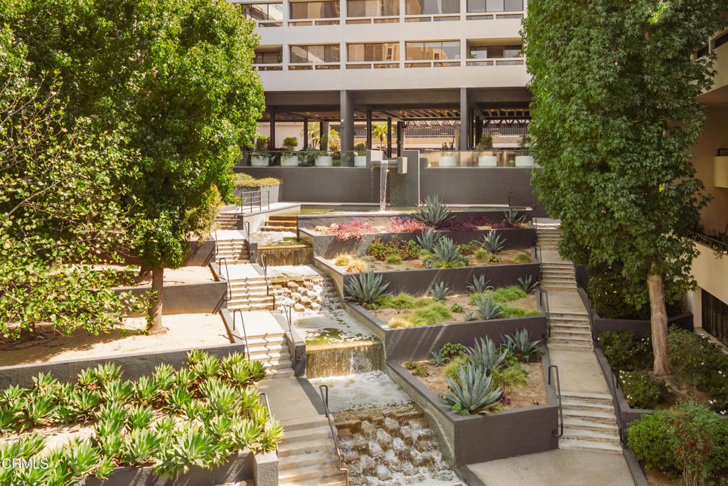 Condominium courtyard with tiered succulent planters, mature trees, and cascading water features.