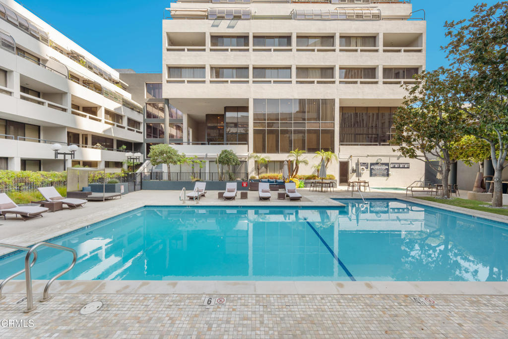Courtyard swimming pool with lounge chairs in front of a multi-story residential building.