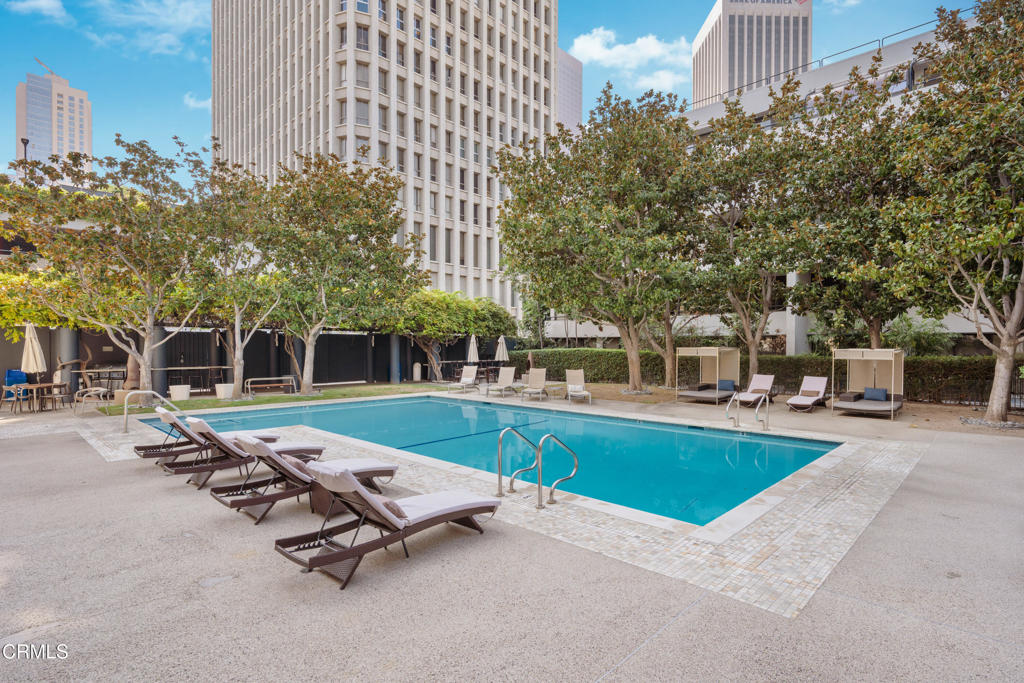 Outdoor swimming pool with lounge chairs and cabanas, surrounded by trees and downtown buildings.