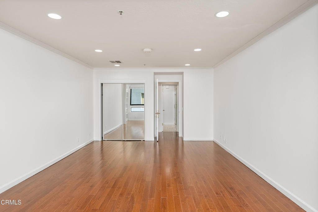 Empty room with hardwood floors, recessed lights, and mirrored sliding closet doors.