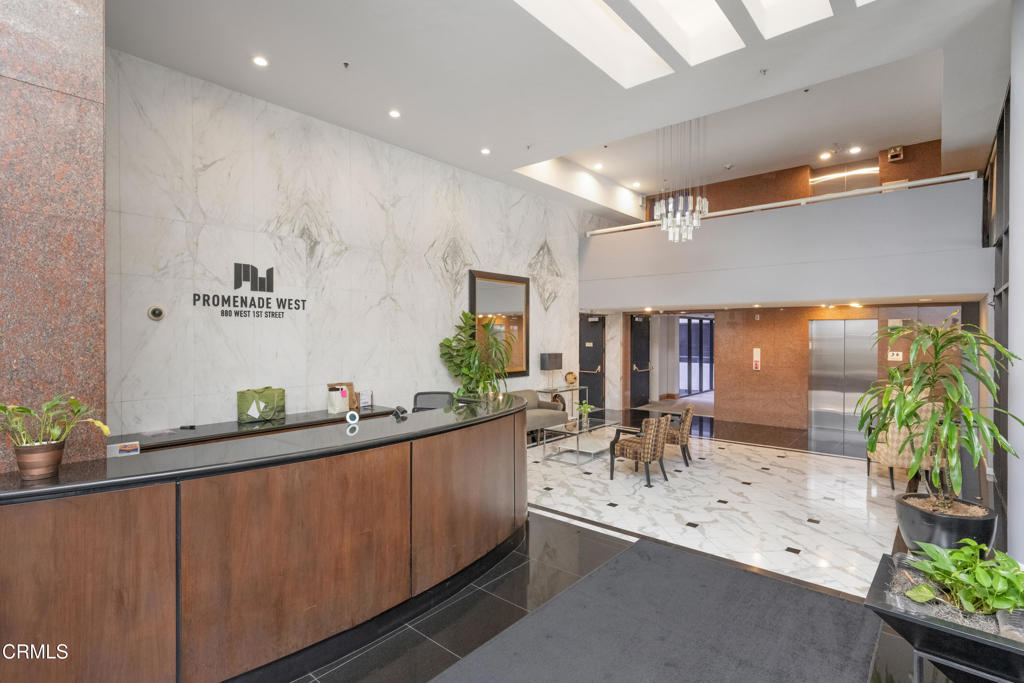 Condominium lobby with a curved wood reception desk, marble walls, elevators, and mezzanine.