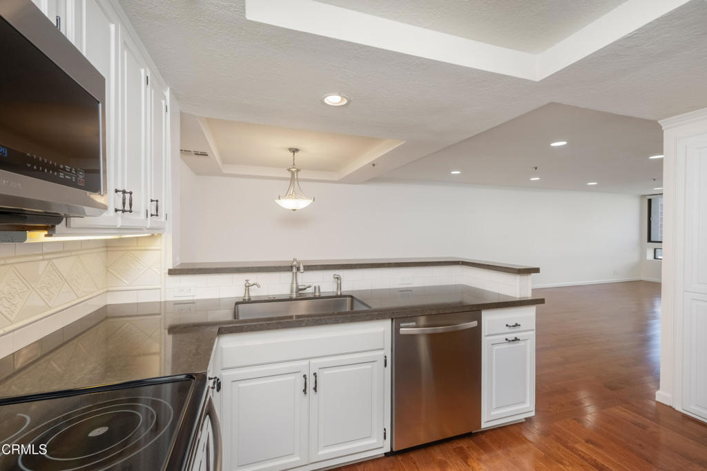 Kitchen with white cabinets, dark stone counters, stainless steel dishwasher, and hardwood floors.