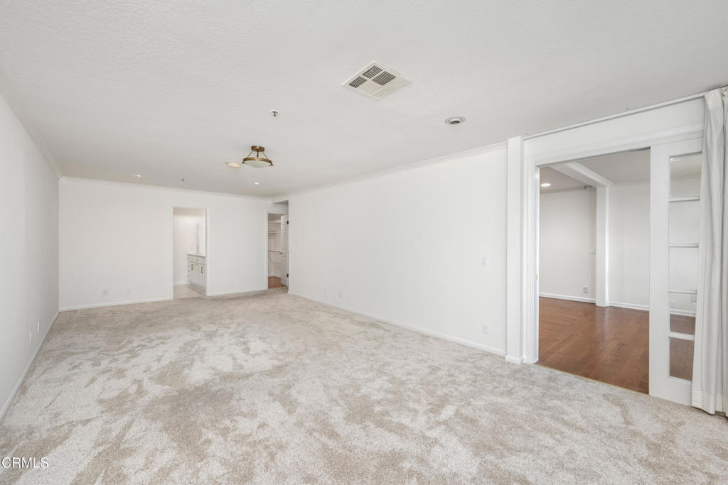 Vacant carpeted room with a wide opening to an adjoining hardwood-floored area.
