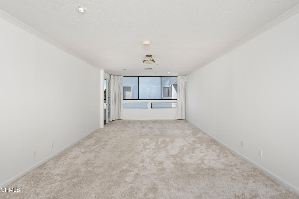 Empty living room with beige carpet and curtained windows at the far end.