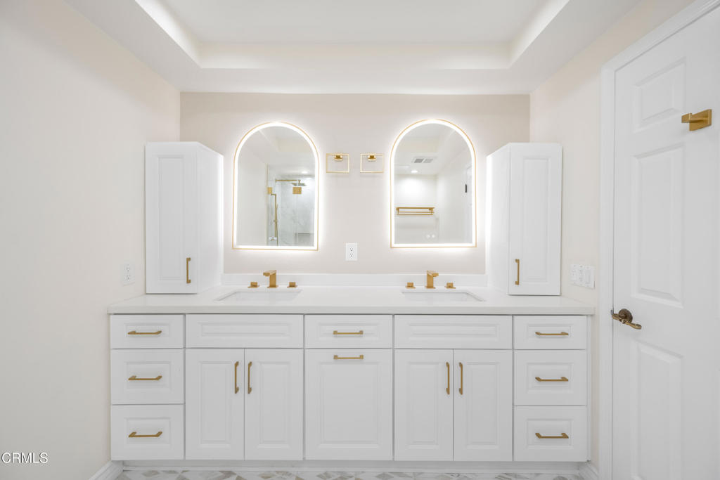 Bathroom with a white double vanity, gold fixtures, and two illuminated arched mirrors.