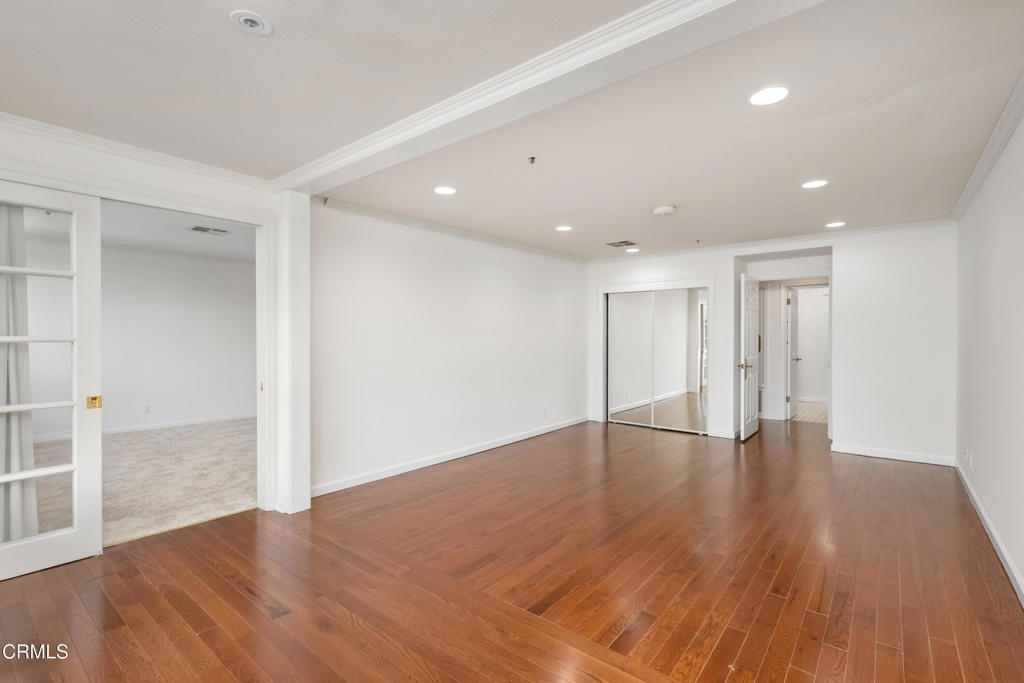 Empty room with hardwood floors, recessed lighting, and mirrored closet doors.