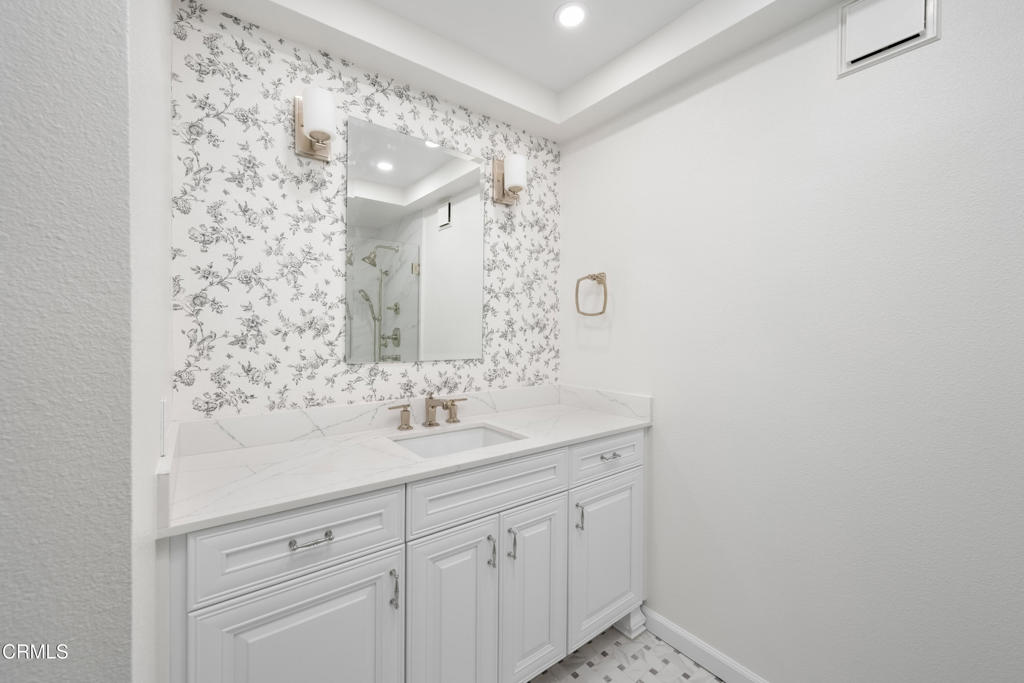 Bathroom vanity with floral wallpaper, a white countertop, and gold-tone fixtures.