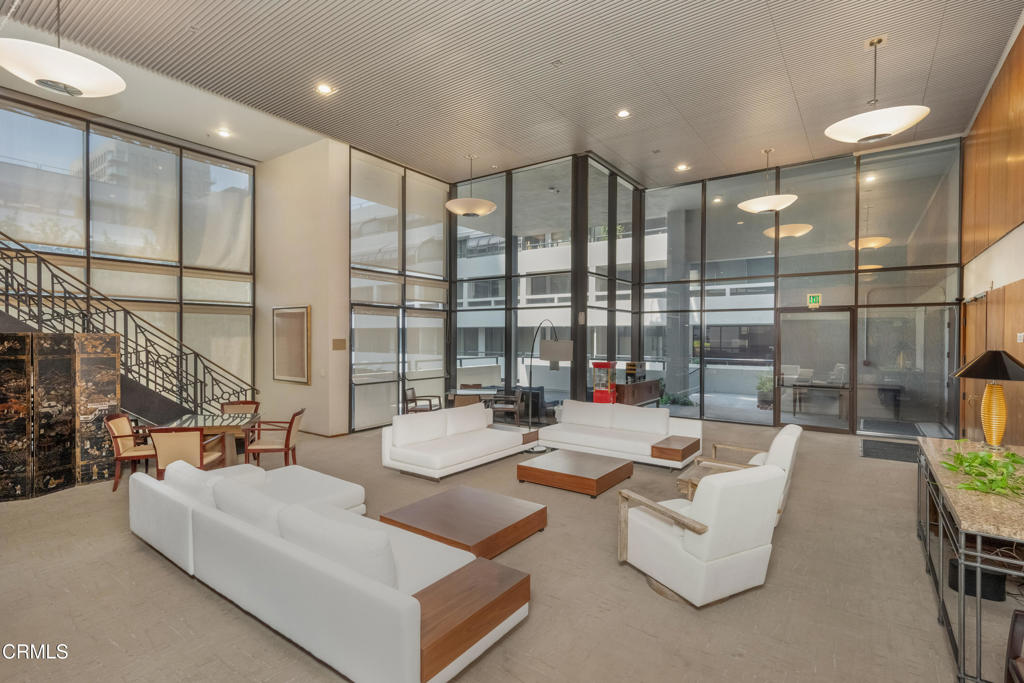 Furnished lobby lounge with white sofas, a staircase, and tall glass walls.
