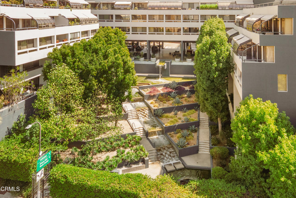 Residential courtyard with mature trees, tiered gardens, stairs, and a cascading water feature.