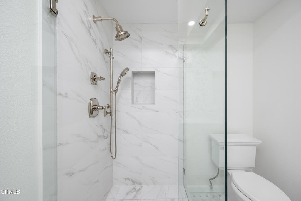 Modern bathroom with a glass shower, marble-look tile, and white toilet.