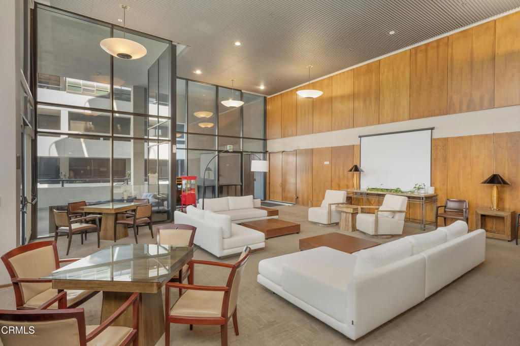 Furnished condominium lounge with white sofas, wood-paneled walls, and floor-to-ceiling glass partitions.