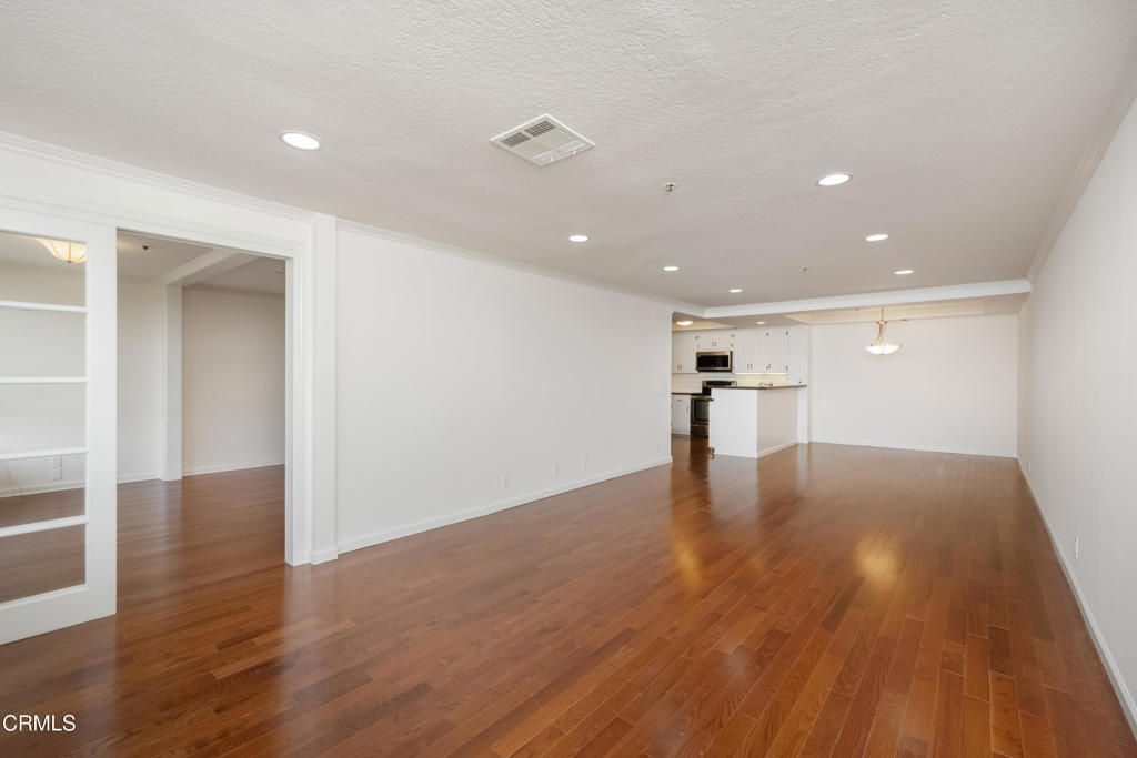 Empty open-plan living area with hardwood floors, built-in shelving, and a kitchen at the far end.