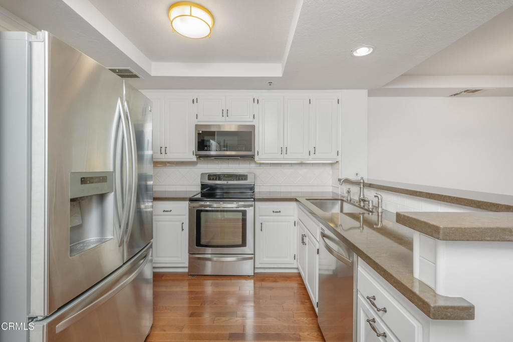 Kitchen with white cabinetry, stainless-steel appliances, beige countertops, and hardwood flooring.