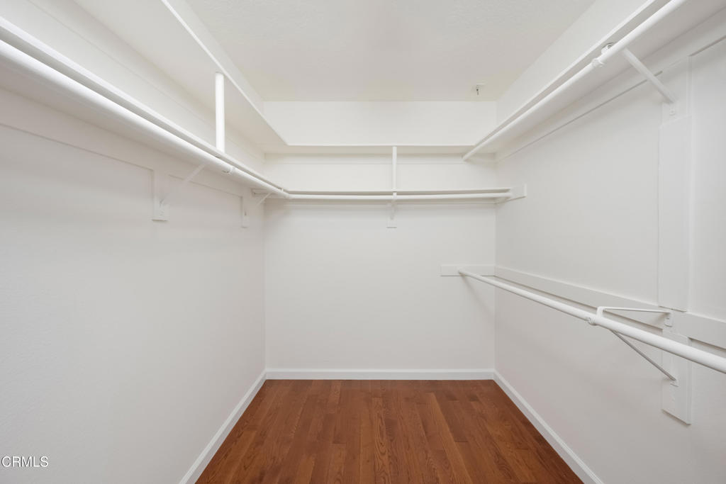 Empty walk-in closet with built-in clothing rods and shelves and a wood floor.