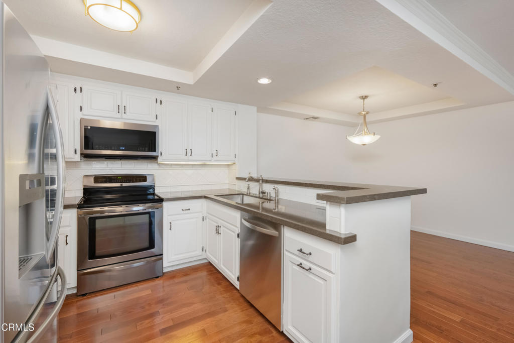 Kitchen with white cabinets, stainless steel appliances, a gray countertop peninsula, and hardwood floors.