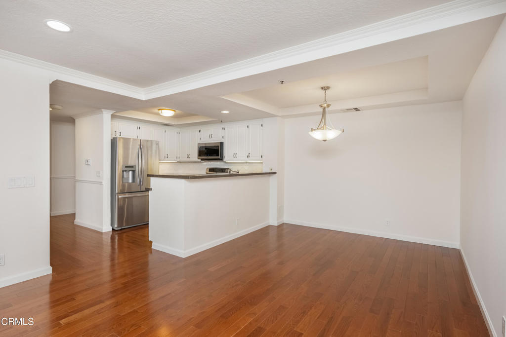 Open kitchen and dining area with white cabinets, stainless steel appliances, and hardwood floors.