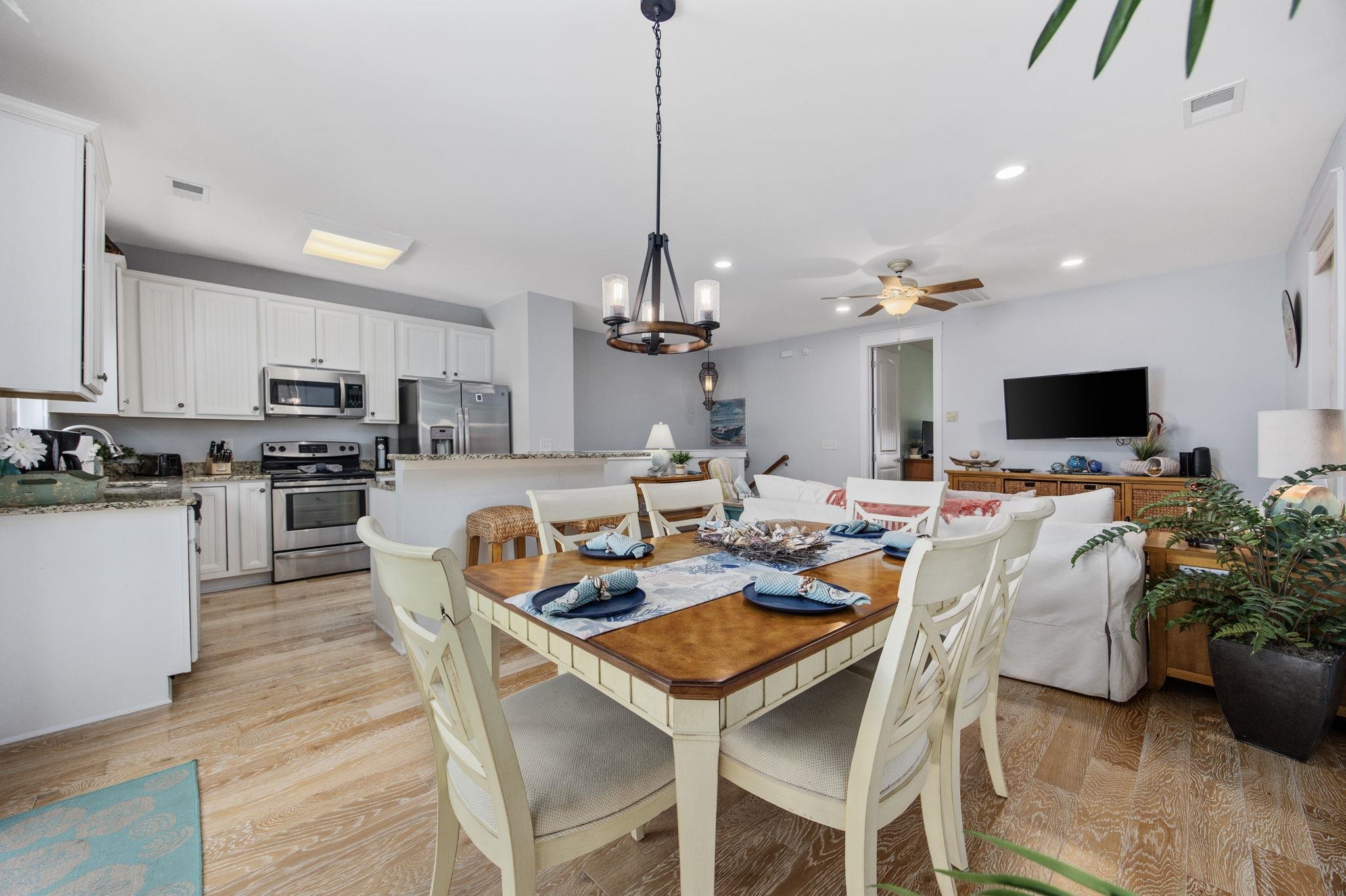 Open-plan dining room with a wooden table, white chairs, and a kitchen with stainless steel appliances.