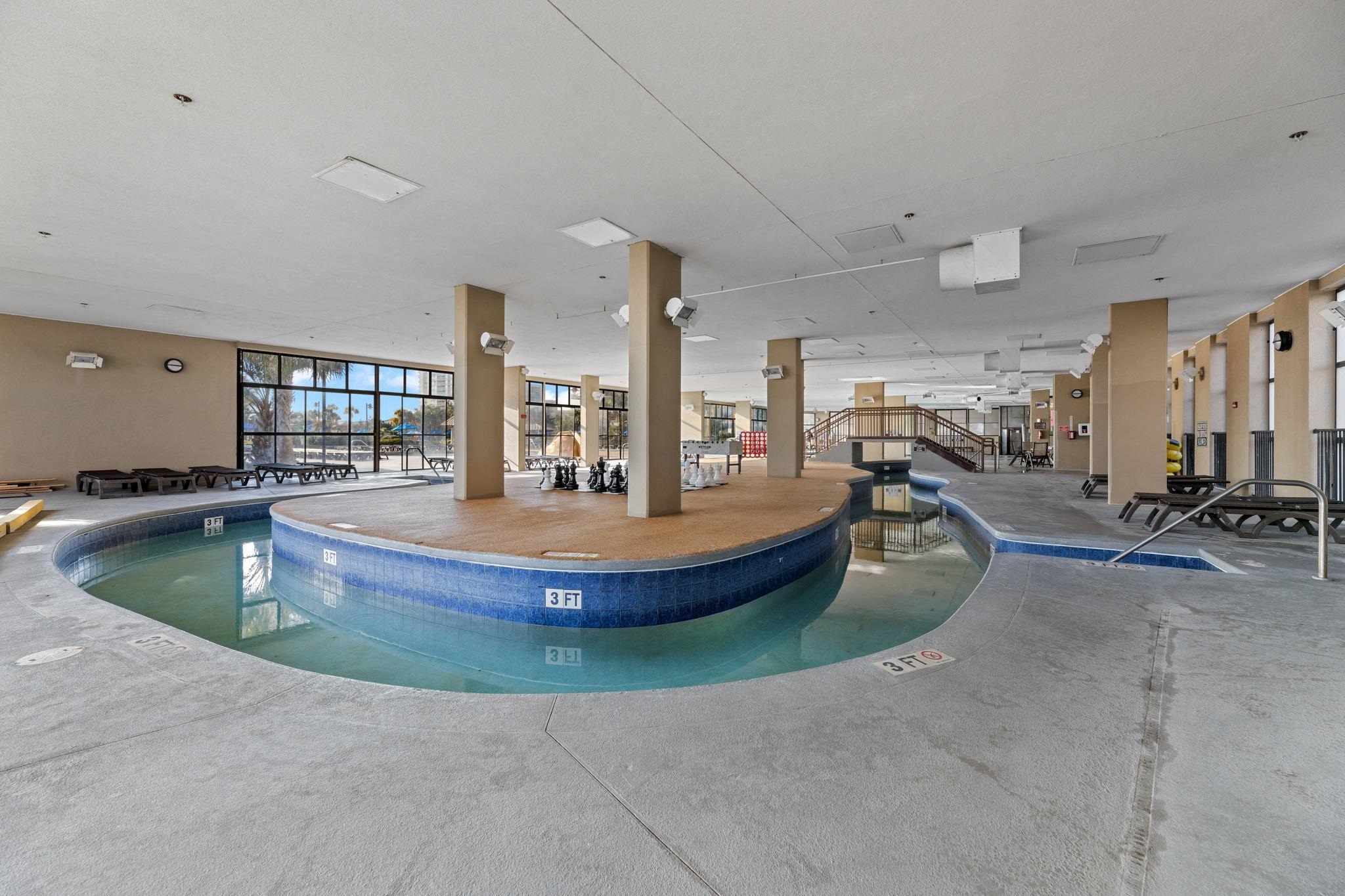Indoor pool with a shallow curved section, blue tile, lounge chairs, and a raised walkway.