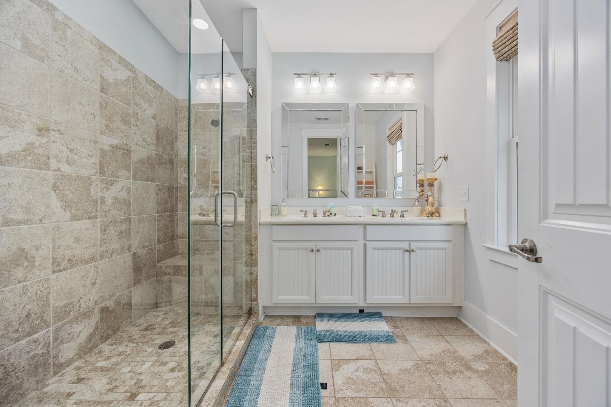 Bathroom with a stone-tiled walk-in shower and white double vanity with two mirrors.