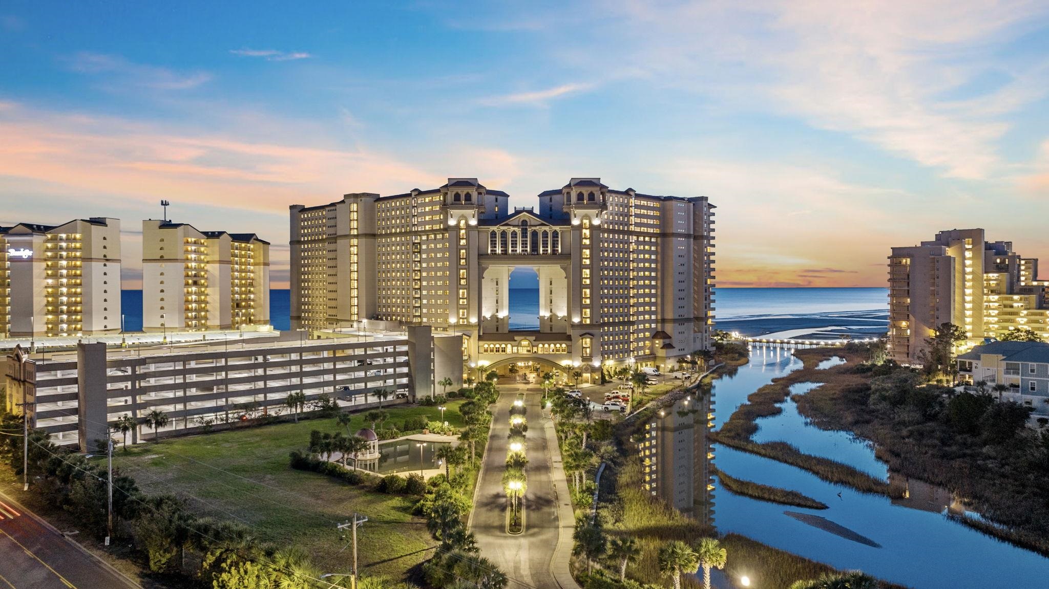 Aerial view of illuminated beachfront high-rises and a coastal inlet at sunset.