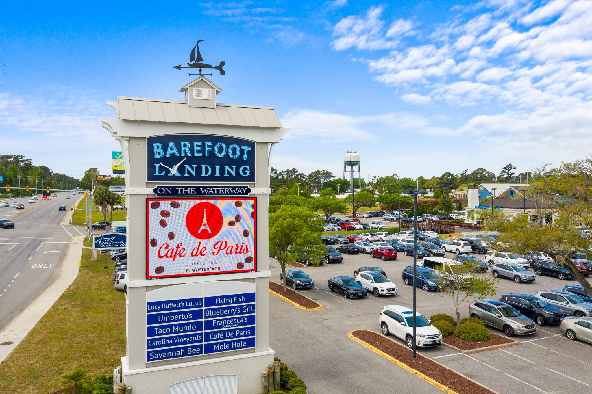 Barefoot Landing sign beside a crowded parking lot, with a Cafe de Paris display.