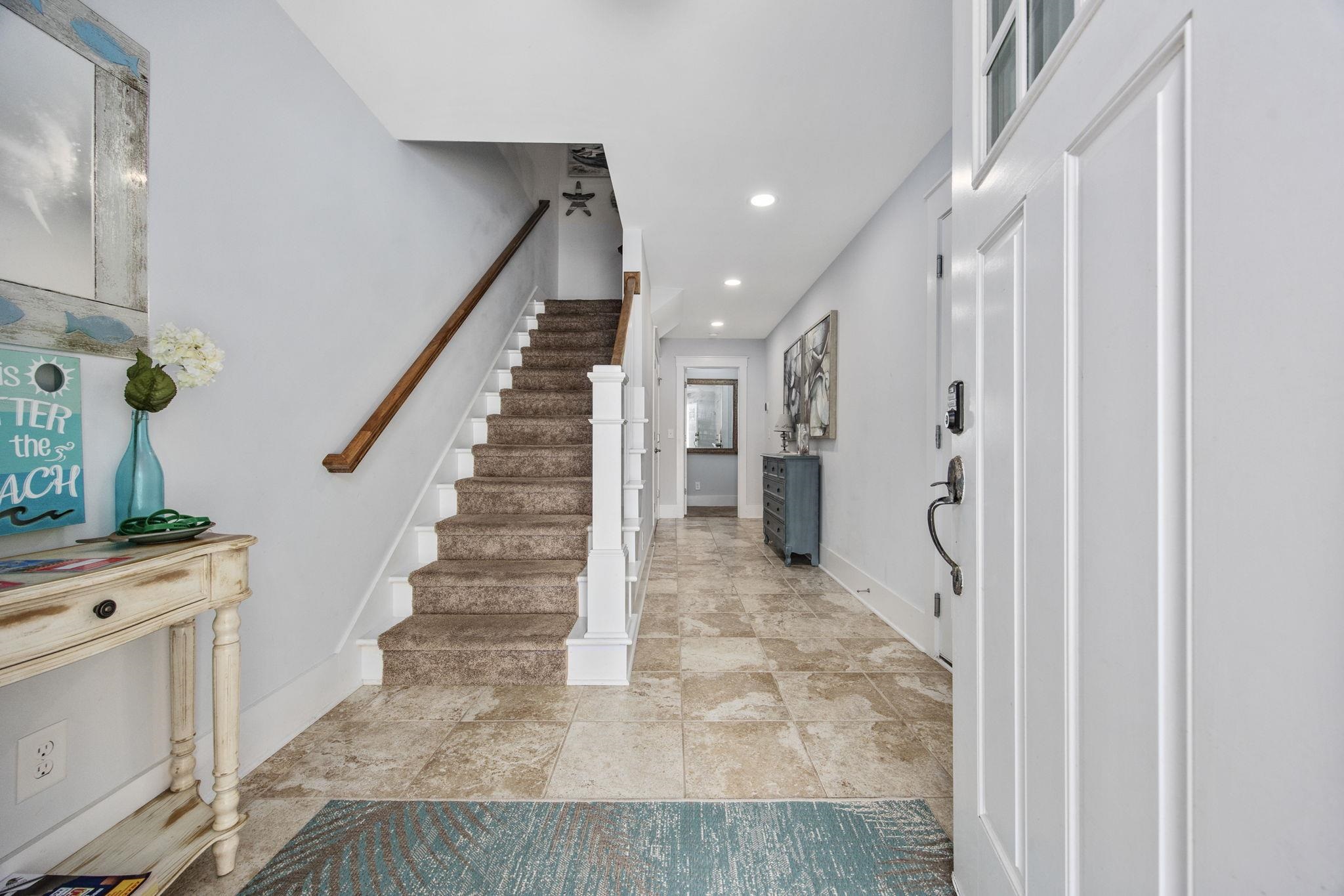 Furnished entry hallway with tiled floors, a carpeted staircase, and a blue rug by the front door.