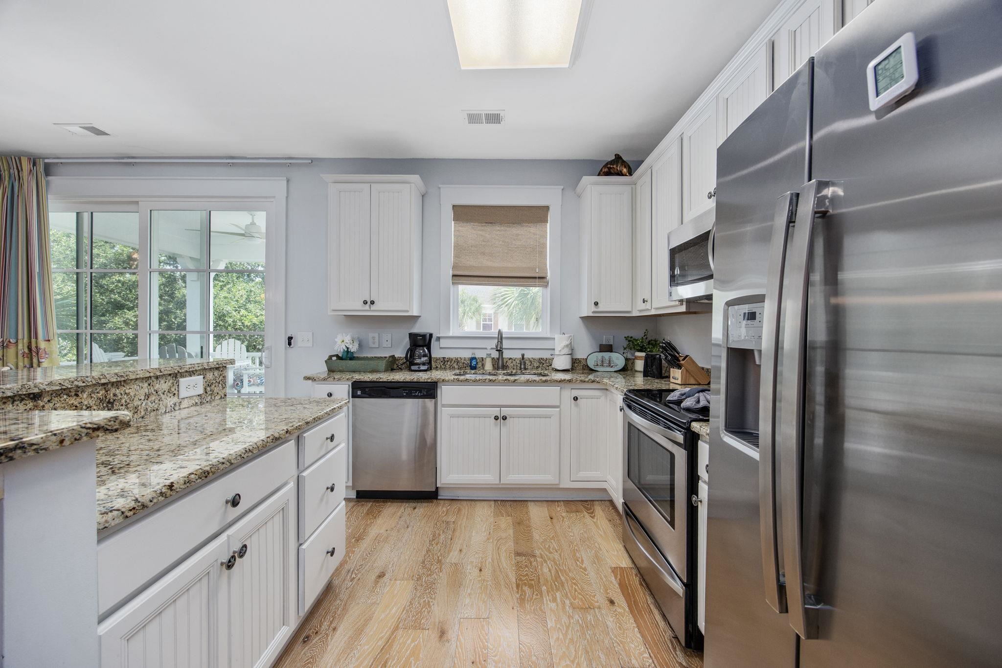 Kitchen with white cabinets, granite counters, stainless steel appliances, and light wood flooring.