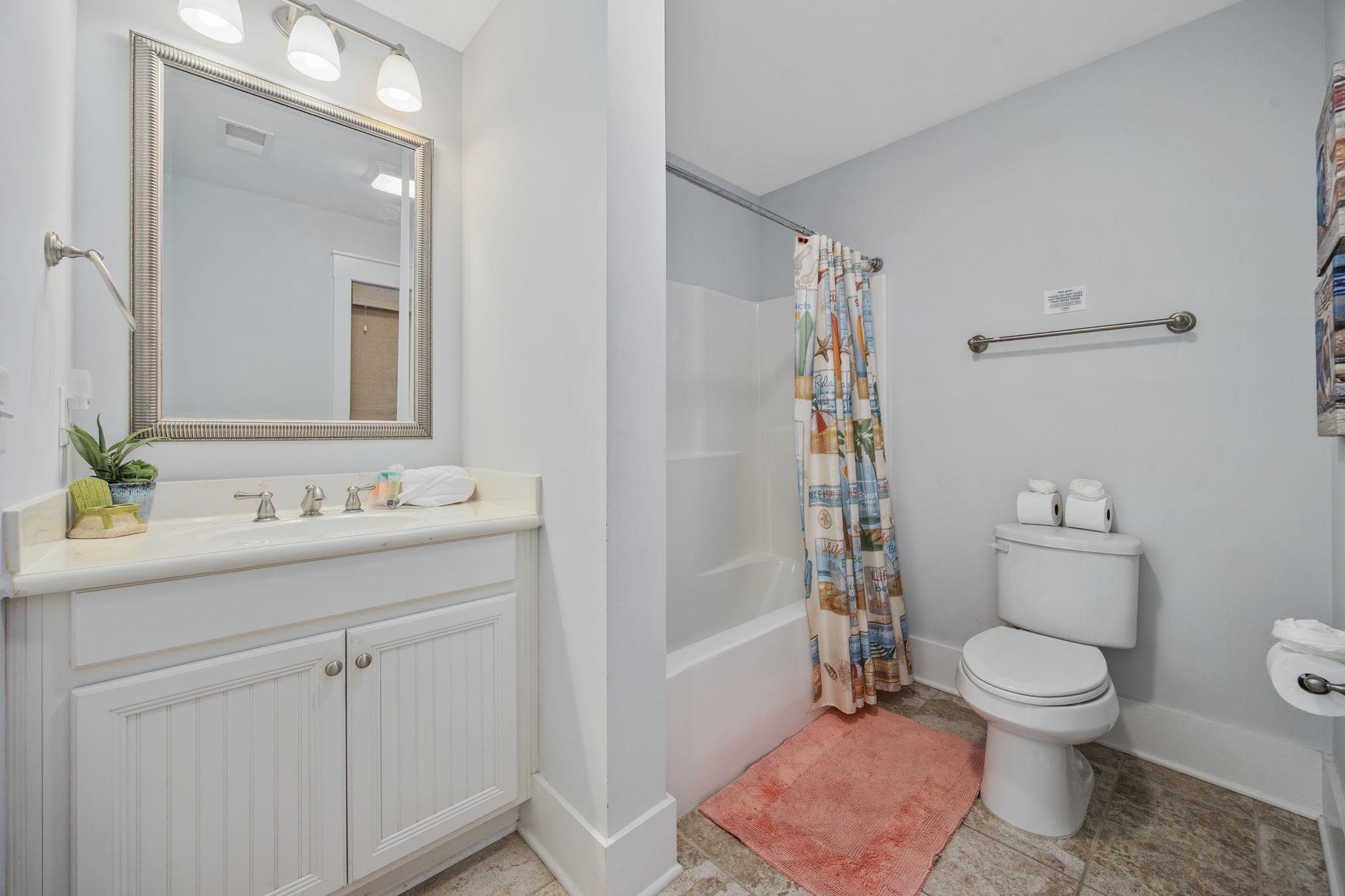 Bathroom with a white vanity, beach-print shower curtain, and coral bath mat.