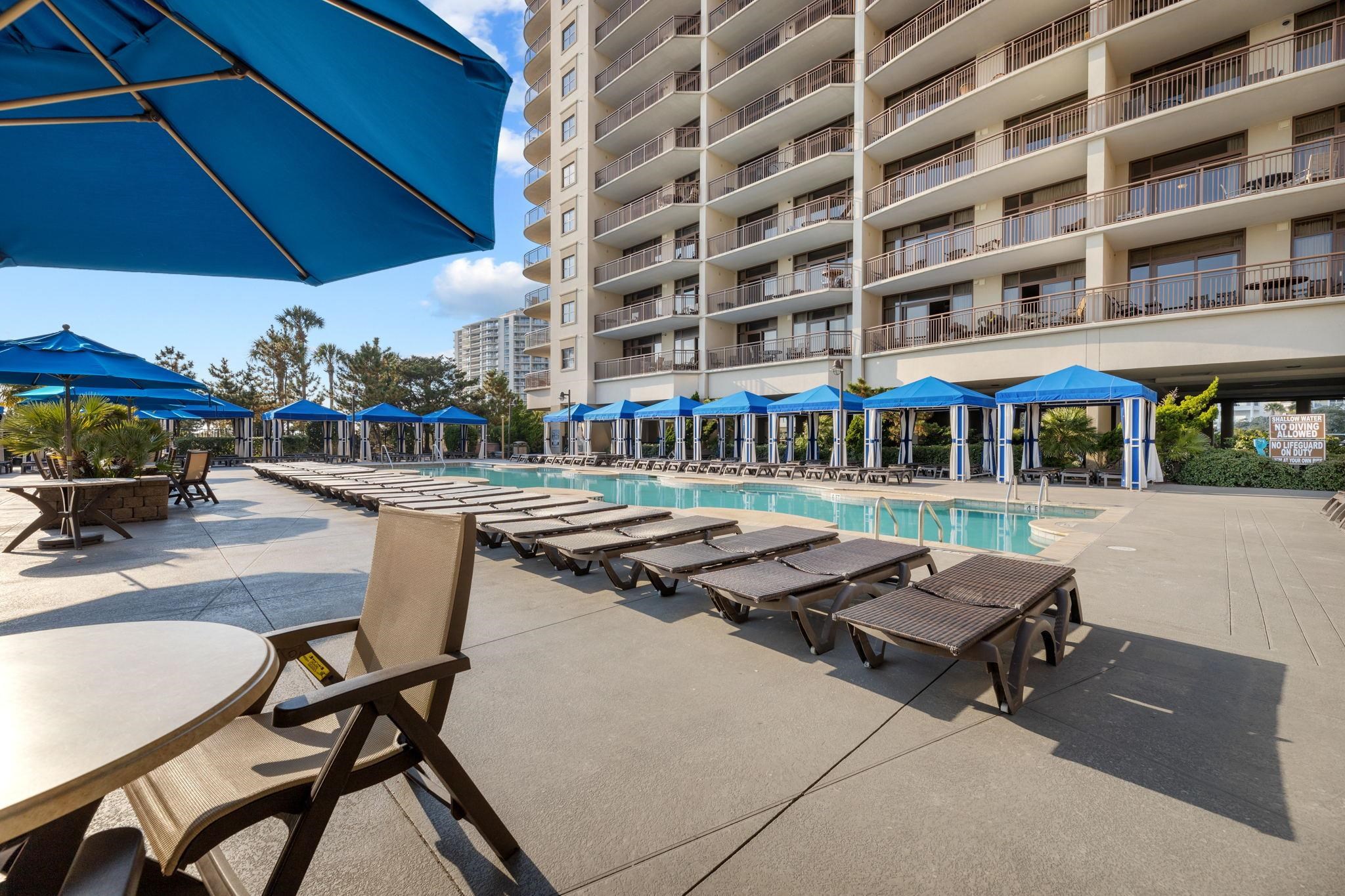Condominium pool deck with rows of loungers and blue cabanas.