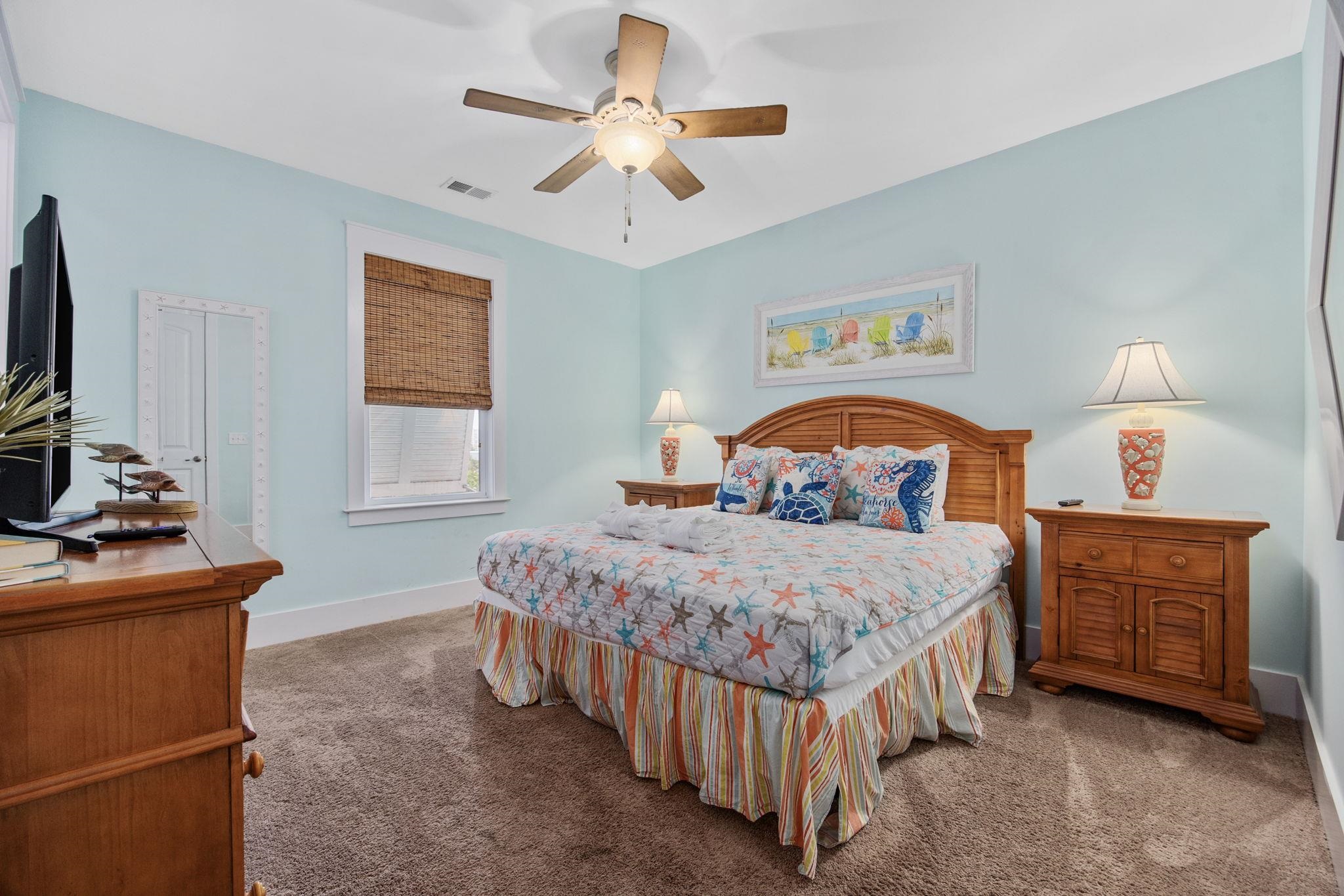 Bedroom with coastal starfish bedding, wooden furniture, pale aqua walls and a ceiling fan.