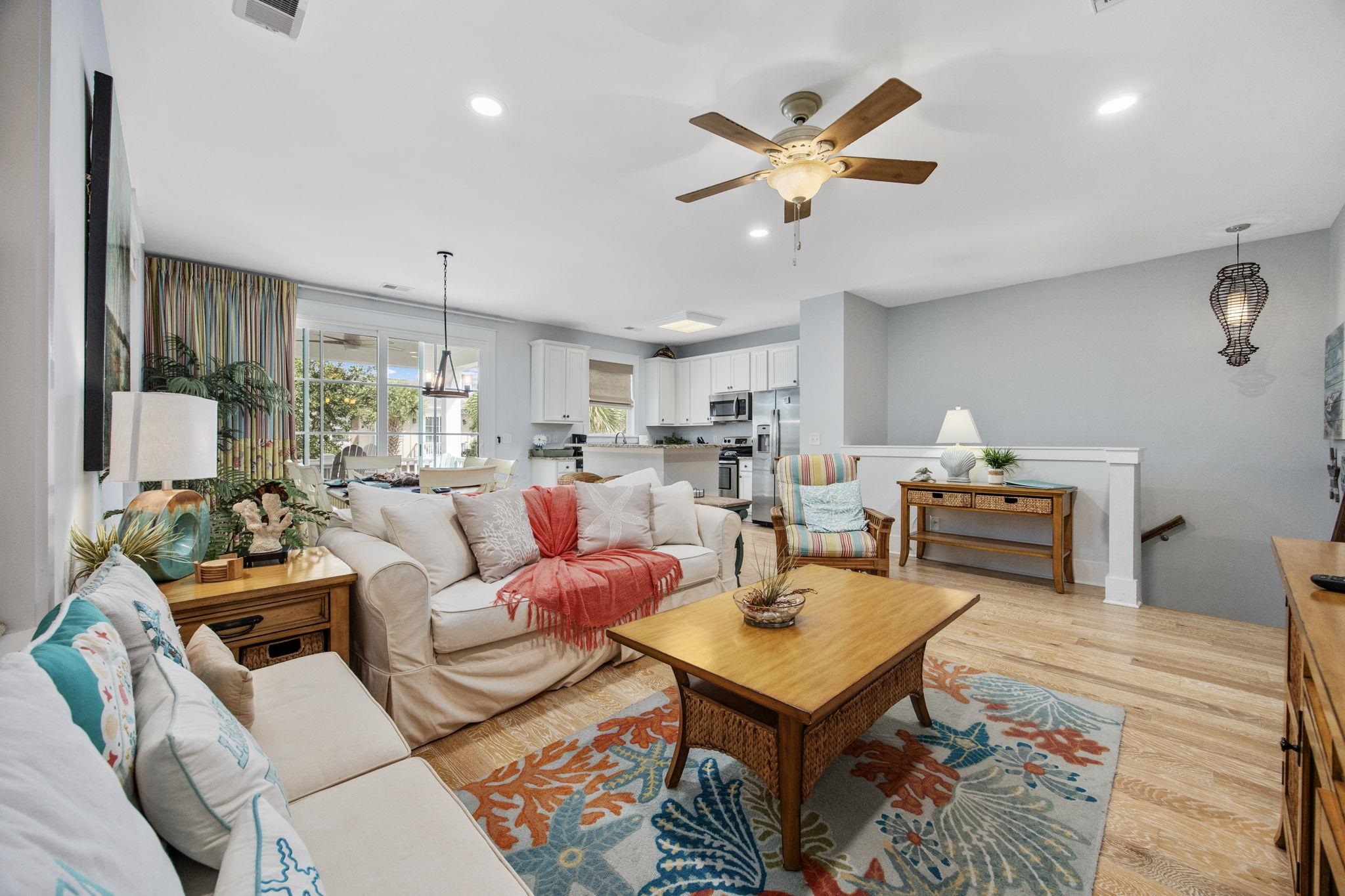Living room with a white sectional, colorful coastal rug, wooden coffee table, and open kitchen.
