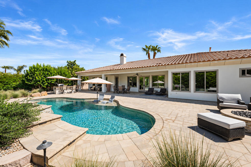 Home with a curved swimming pool and furnished stone patio beneath a terracotta tile roof.